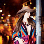 99px.ru аватар Девушка в широкополой шляпе, с длинными распущенными волосами стоит у рекламного столба на вечерней улице города