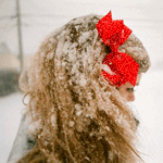 Аватар Белокурая девушка с красным бантом в волосах стоит под падающим снегом
