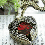 99px.ru аватар Кулон с красным камнем виде сердца, прикрытого крыльями ангела на цепи, лежащий на фоне печатного текста