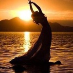 99px.ru аватар Девушка в длинном платье стоит в морской воде, подняв руки вверх. За девушкой видны горы и заходящее солнце