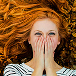 99px.ru аватар Рыжеволосая девушка лежит на осенних листьях, смеется, прикрыв лицо ладонями