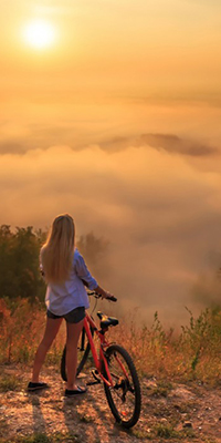 99px.ru аватар Девушка с велосипедом стоит на высокогорье и смотрит, как на восходе солнца стелется утренний туман и рваными клочьями расползается между деревьев по лощине