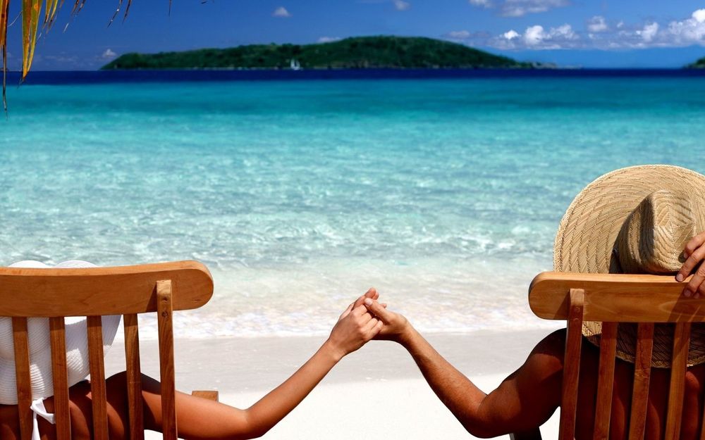 Обои для рабочего стола Мужчина и девушка держатся за руки на берегу моря лежа в деревянных шезлонгах