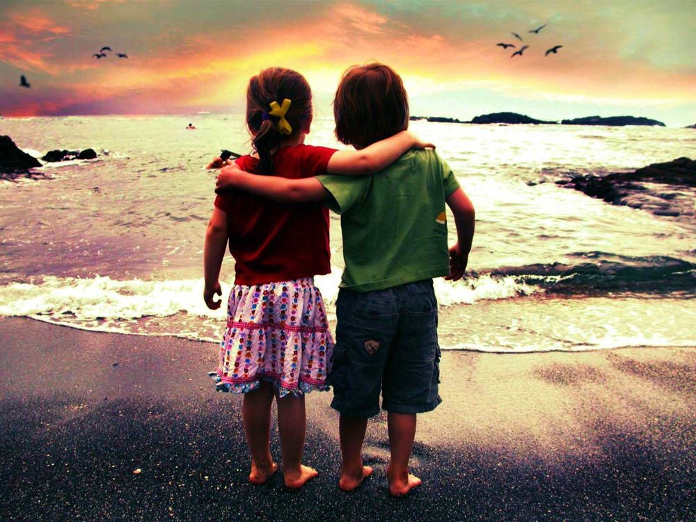 Обои для рабочего стола Мальчик и девочка стоят в обнимку у моря и смотрят на закат