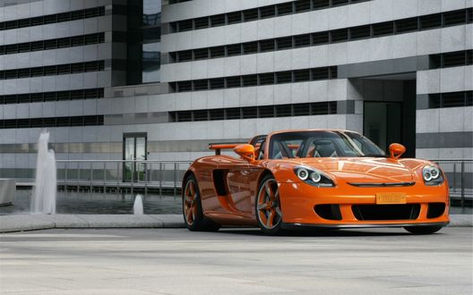 Обои на рабочий стол Porsche TE CGT / Порше оранжевого цвета стоит у здания