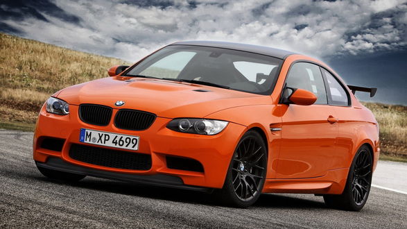 Обои на рабочий стол БМВ / BMW оранжевого цвета стоит на дороге в поле