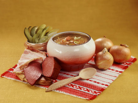 Обои на рабочий стол Русская кухня - горшочек с солянкой, рядом продукты для её приготовления: репчатый лук, солёные огурцы и копчённости
