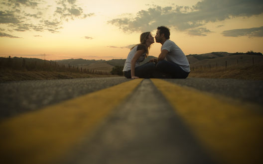 Обои на рабочий стол Парень и девушка целуются сидя на закате на разделительной полосе на дороге