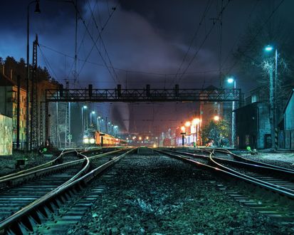 Обои на рабочий стол Железнодорожные пути проходящие через дома подсвеченные фонарями ночью