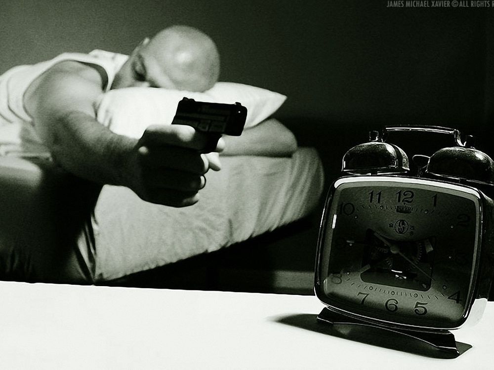 Обои для рабочего стола Мужчина направил на будильник пистолет, явно не желая просыпаться