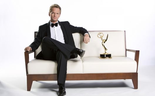 Обои на рабочий стол Актер Нил Патрик Харрис / Neil Patrick Harris в костюме с бабочкой сидит на белом диване возле награды