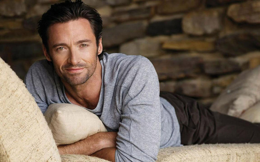 Обои для рабочего стола Актер Хью Джекман / Hugh Jackman лежит на диване соломенного цвета