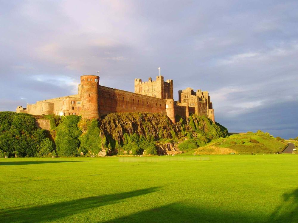 Обои для рабочего стола Замок Бамбург / Bamburgh Castle на горе, окруженный зеленым лугом, графство Нортумберленд / Northumberland, Великобритания