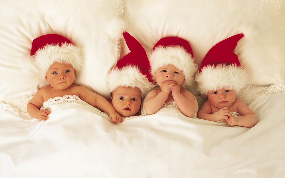 Обои для рабочего стола Начинающие Деды Морозы - смешные младенцы в новогодних шапках лежат под одеялом в постели