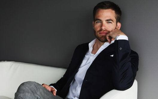 Обои на рабочий стол Голубоглазый Крис Пайн / Chris Pine сидит на белом диване в пиджаке и джинсах и смотрит прямо в камеру