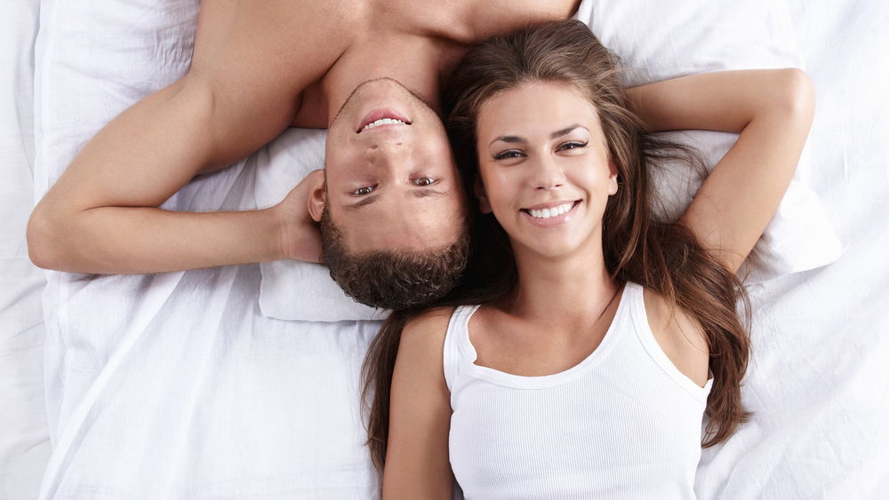 Обои для рабочего стола Счастливые парень и девушка лежат валетом на кровати и улыбаются