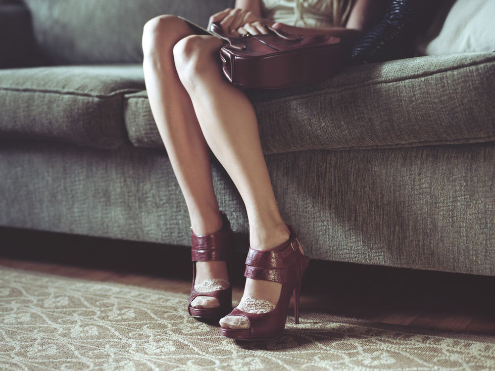 Обои для рабочего стола Девушка сидит на диване в коричневых туфлях и с сумочкой в тон