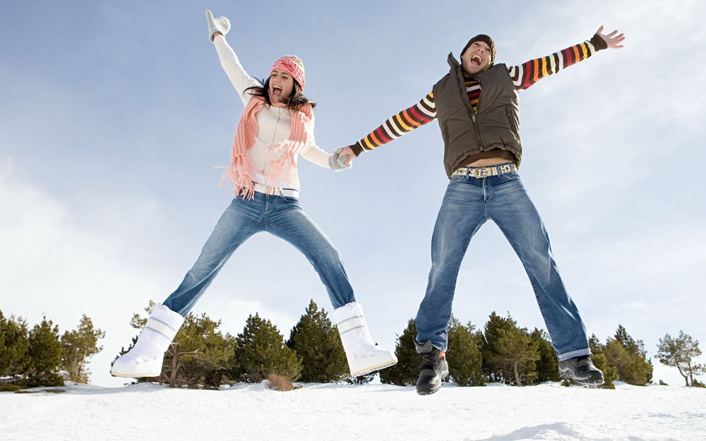 Обои для рабочего стола Парень и девушка радостно скачут по снегу возле леса