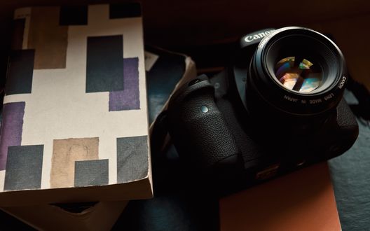 Обои на рабочий стол Фотоаппарат Canon рядом со стопкой книг