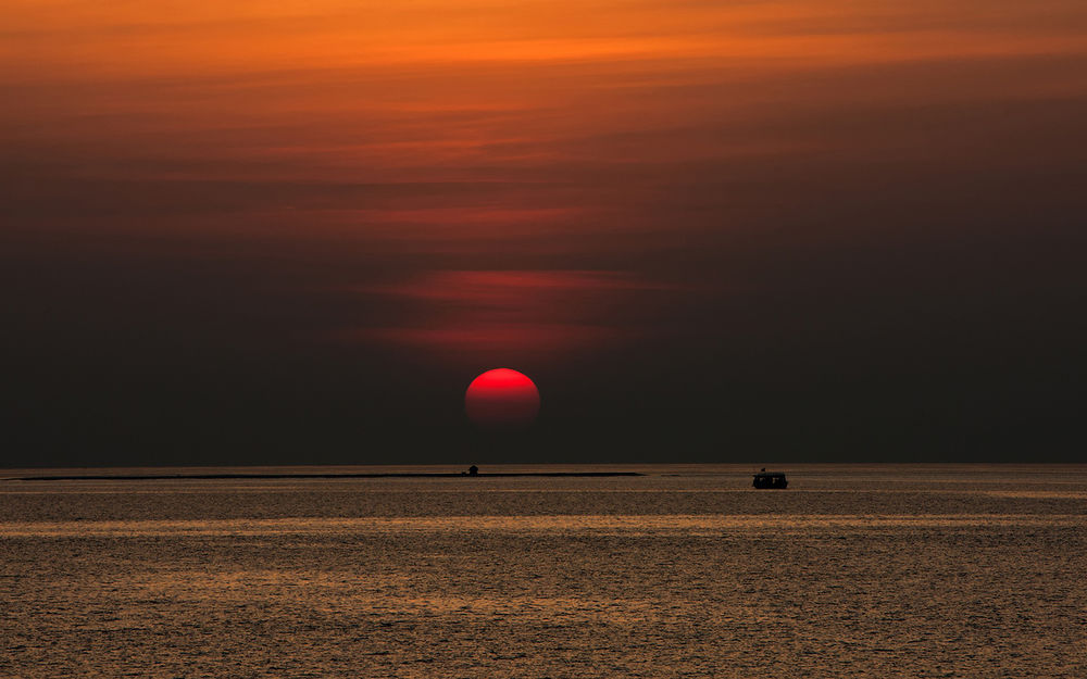 Обои для рабочего стола Красный диск солнца медленно заходит за горизонт моря