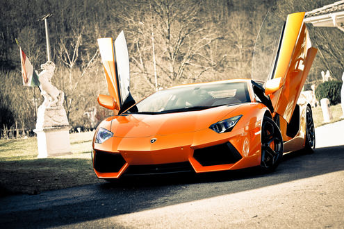 Обои на рабочий стол Оранжевая Lamborghini Aventador, LP700-4 / Ламборгини Авентадор с поднятыми дверьми среди статуй