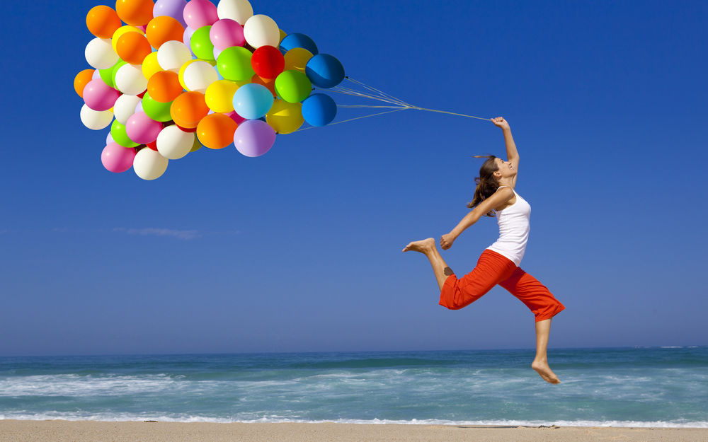 Обои для рабочего стола Девушка с разноцветными шарами в прыжке на пляже