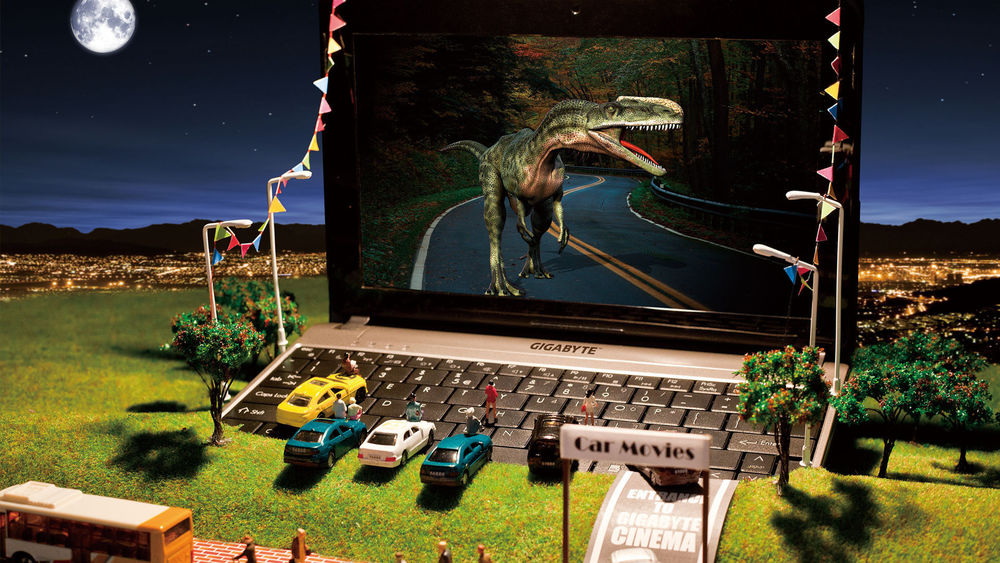 Обои для рабочего стола Ноутбук вкопан в землю, вокруг него игрушечные машины и человечки, на экране ноутбука фильм про динозавров (Car movies)