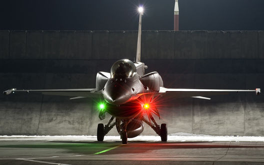 Обои на рабочий стол Американский истребитель F-16 с включенными бортовыми фарами  готовится вырулить на взлетно-посадочную полосу для совершения полета в ночных условиях