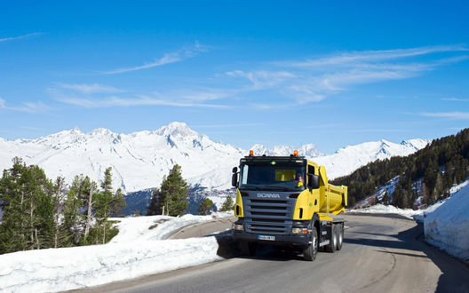Обои на рабочий стол Желтый тягач Scania / Скания едет по дороге среди снежных гор и елок
