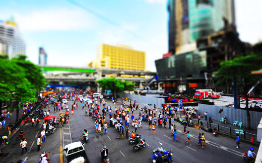 Обои на рабочий стол Ratchaprasong Road в городе Bangkok, Thailand / Бангкок, Таиланд с улицей, заполненной большим количеством людей и автотранспорта, на фоне небосребов и деревьев с зеленой листвой, с эффектом тилт шифт / tilt shift