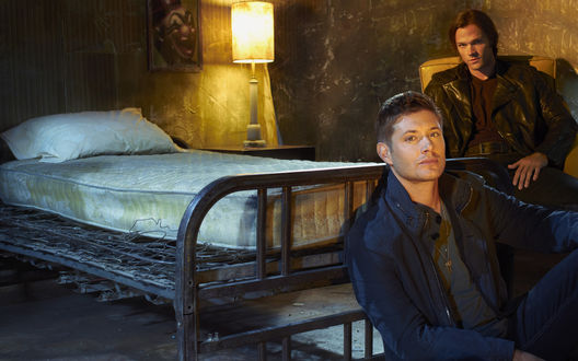 Обои на рабочий стол Sam/ Сэм и  Dean / Дин Винчестеры /  Winchester из сериала Сверхъестественное / Supernatural, актеры Джаред Падалеки / Jared Padalecki и Дженсен Эклз / Jensen Ackles сидят в дешевой гостинице