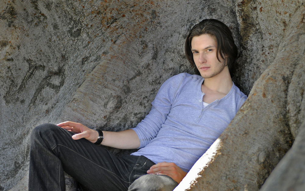 Обои для рабочего стола Актер Бен Барнс / Ben Barnes сидит у каменной стены