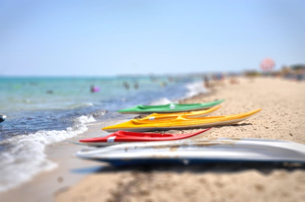 Обои для рабочего стола Тунис, пляж на морском побережье, на светло-коричневом песке которого, находится несколько разноцветных байдарок, на фоне голубого, безоблачного неба, с эффектом тилт шифт / tilt shift