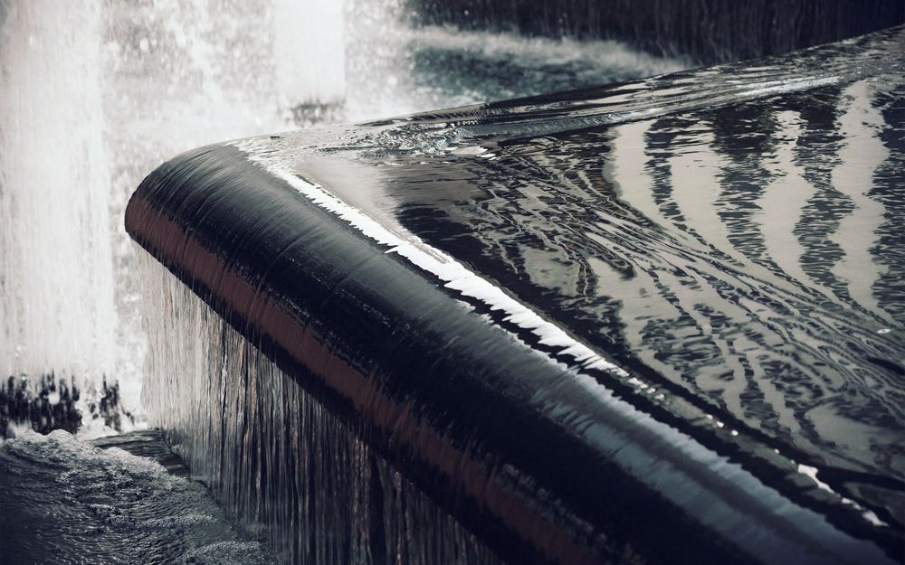 Обои для рабочего стола Вода стекает по чёрной гладкой поверхности фонтана, образуя искусственный водопад