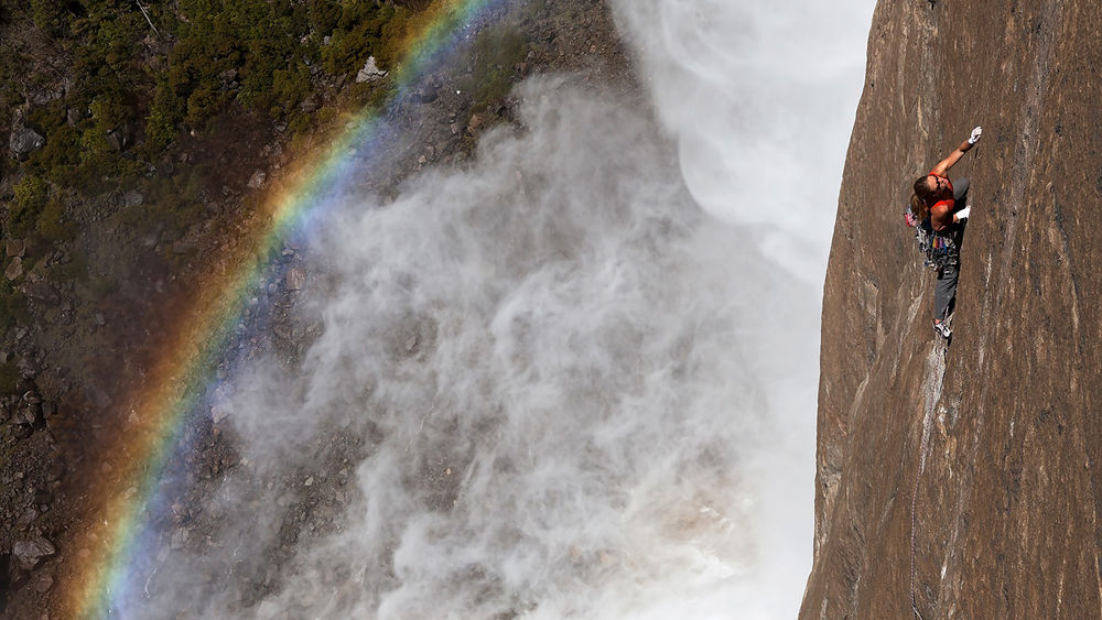Обои для рабочего стола Альпинист взбирается по скале вдоль водопада, а под ним образуется яркая радуга, Йосемитский национальный парк, штат Калифорния, США / Yosemite National Park,California, USA