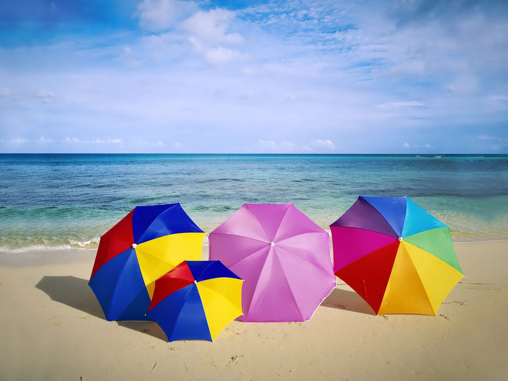 Обои для рабочего стола Разноцветные зонтики лежат на песке морского берега на фоне неба с перистыми облаками