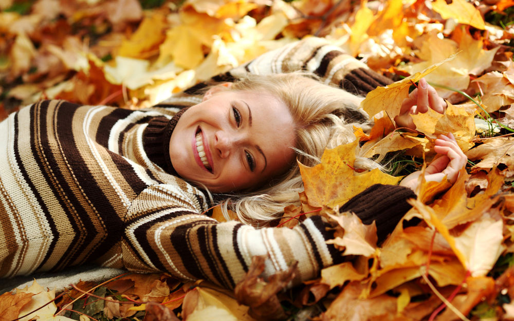Обои для рабочего стола Улыбающаяся девушка лежит в осенних листьях
