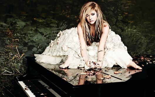 Обои на рабочий стол Знаменитая пианистка Аврил Лавин, Канада  / Avril Lavigne, Canada в белом, длинном платье, босая, сидит на черном рояле на фоне зеленых листьев