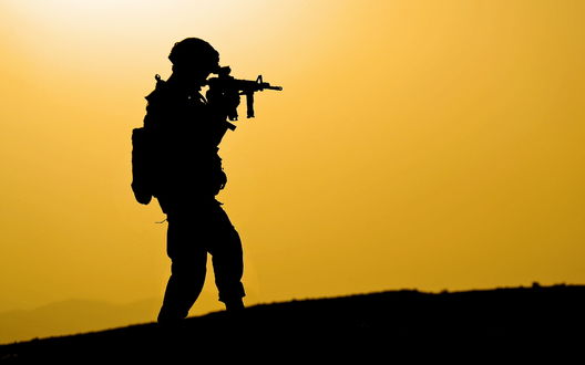 Обои на рабочий стол Силуэт американского военного на фоне желтого неба в каске с автоматическим оружием в руках