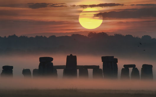 Обои на рабочий стол Каменное мегалитическое сооружение Стоунхендж / Stonehenge в предрассветной туманной дымке и огромный желтый диск солнца