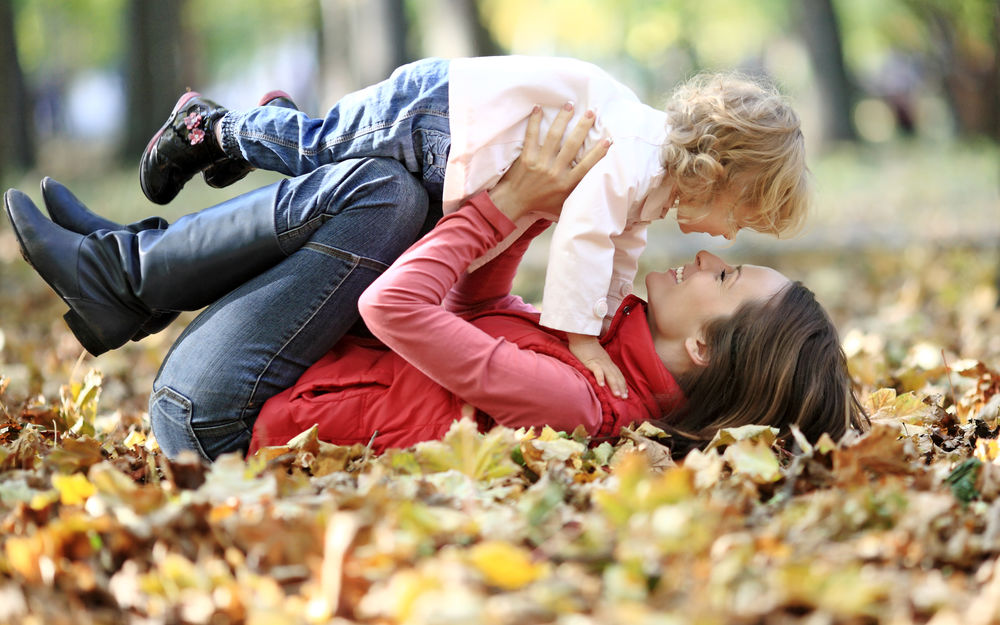 Обои для рабочего стола Счастливая мама с ребенком резвятся в парке на осенних листьях