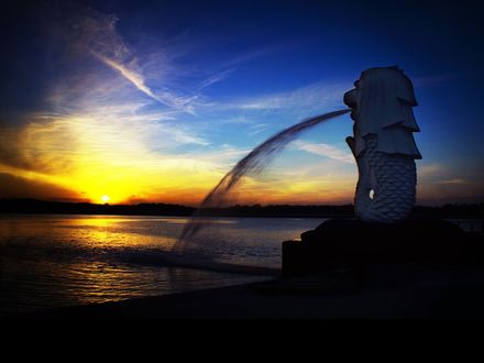 Обои на рабочий стол Фонтан со статуей Мерлион / Merlion - морской лев в Сингапуре / Singapore в свете заходящего солнца