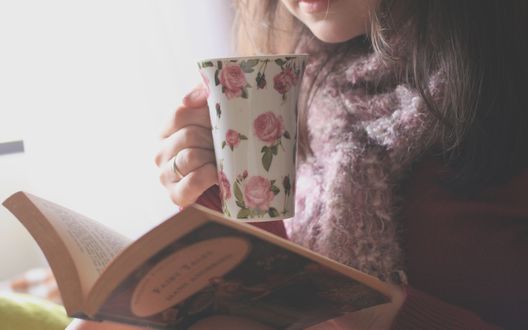 Обои на рабочий стол Девушка с чашкой в руке читает книгу
