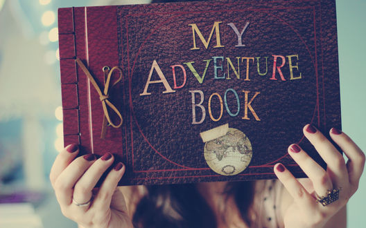 Обои на рабочий стол Девушка держит в руках книгу с надписью My adventure book / Моя книга путешествий