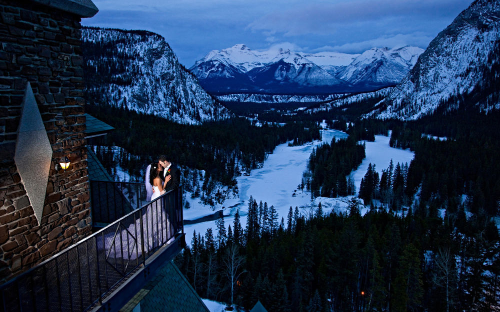 Обои для рабочего стола Молодожены стоят в обнимку на балконе отеля, расположенного в горах