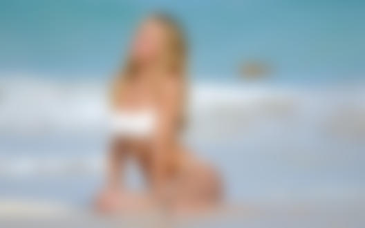 Обои для рабочего стола Candice Swanepoel / Кэндис Свейнпол в белом купальнике сидит на берегу моря, волны бьются о ее стройные ноги