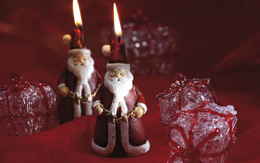 Обои на рабочий стол Игрушечные Санта-Клаусы / Santa Claus с горящими свечами на голове, в окружении новогодних подарков в блестящих коробках