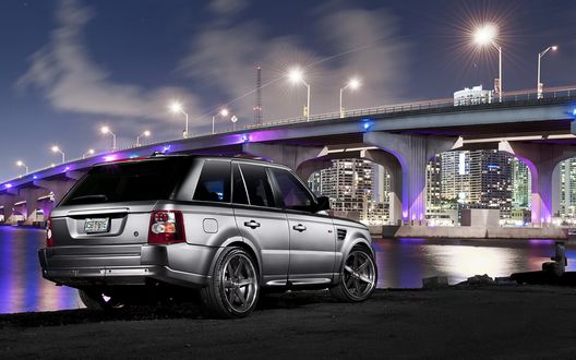 Обои на рабочий стол Серебристый Range Rover ночью стоит у реки под мостом в свете городских фонарей