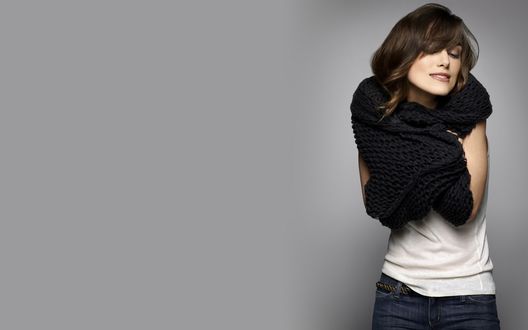 Обои на рабочий стол Британская актриса Кира Найтли / Keira Knightley в джинсах, белой футболке и закутавшаяся в шарф, стоит на сером фоне