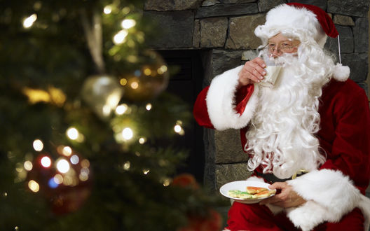 Обои на рабочий стол Санта Клаус / Santa Claus пьет молоко и ест печенье возле новогодней ёлки